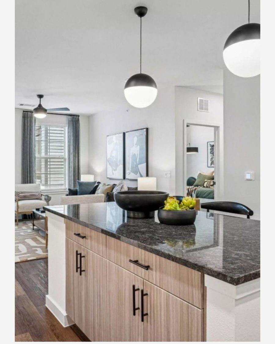 Open apartment kitchen with dark granite island and globe pendant lights